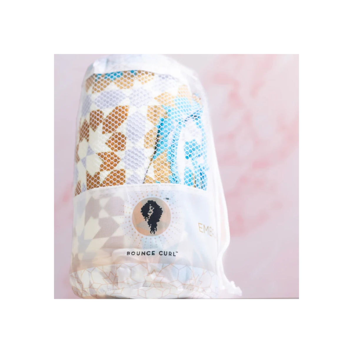 Farverigt Bounce Curl Micro-fiber Towel i netpose med geometrisk mønster og logo foran rosa baggrund.