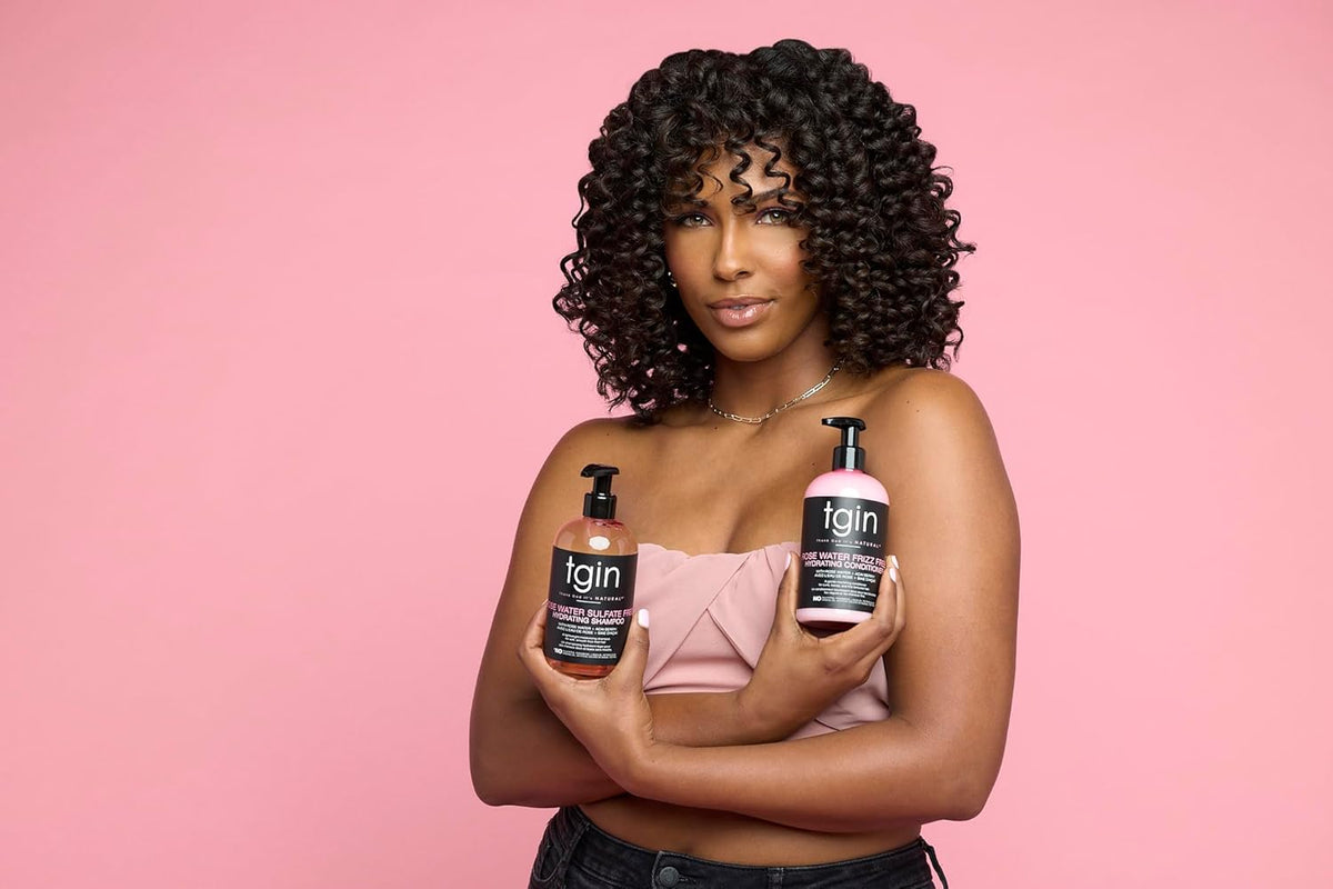 Kvinde med krøllet hår holder TGIN Rose Water Shampoo 384ml og conditioner foran lyserød baggrund.